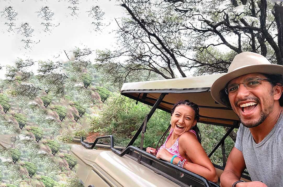 Two smiling travellers leaning out of an open-roof safari vehicle